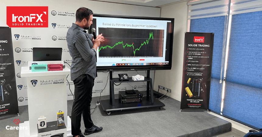 A man presenting on a screen, pointing at charts and graphs during a business meeting.