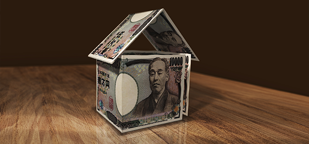 A table displays a house made entirely of money, representing Japan's real estate market.