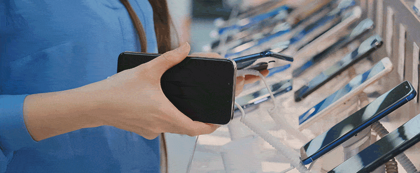 A person holding a cell phone in front of a rack of cell phones, showcasing the latest mobile devices