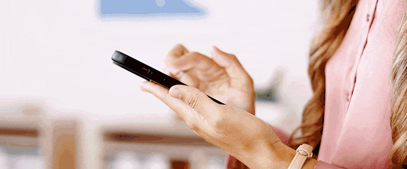 A woman holding a cell phone in her hand, engaged in conversation or browsing content on the device.
