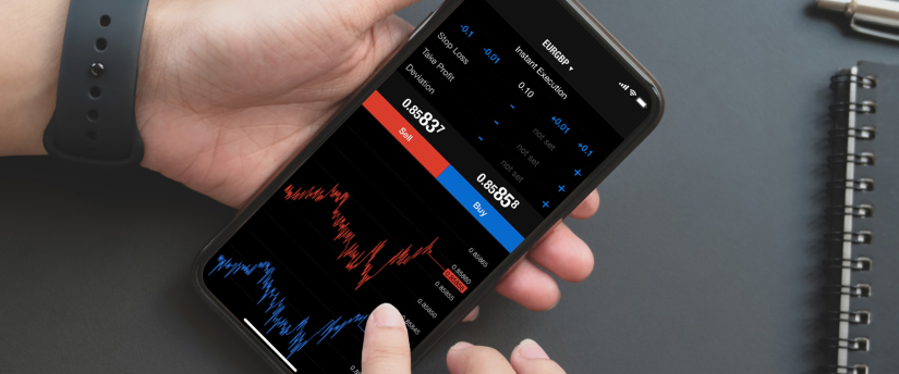 Hand holding a smartphone displaying a MetaTrader trading screen with price charts and buy/sell options.
