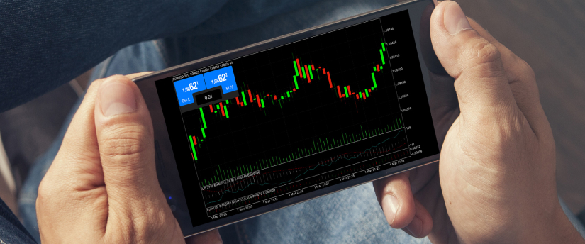 Hands holding a smartphone showing a forex trading chart with candlesticks, market data and Tesco share price analysis.