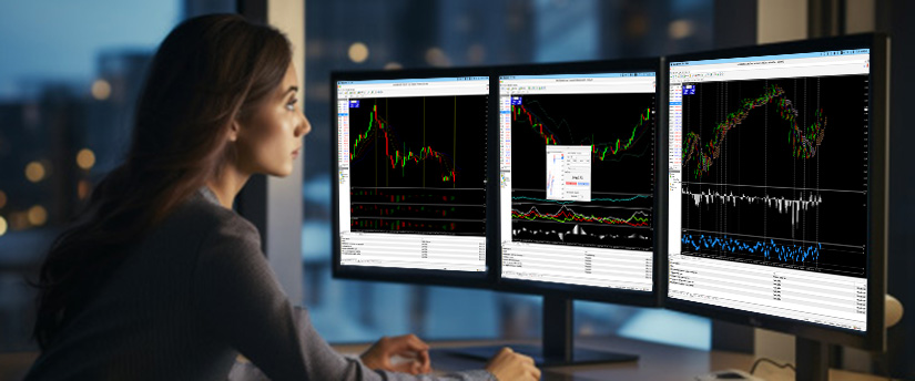 Woman analyzing multiple demo trading charts on three computer monitors in a modern office setting at night