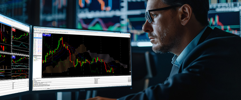 A male financial analyst studying currency pair trading signals on a multi-monitor trading station at night.