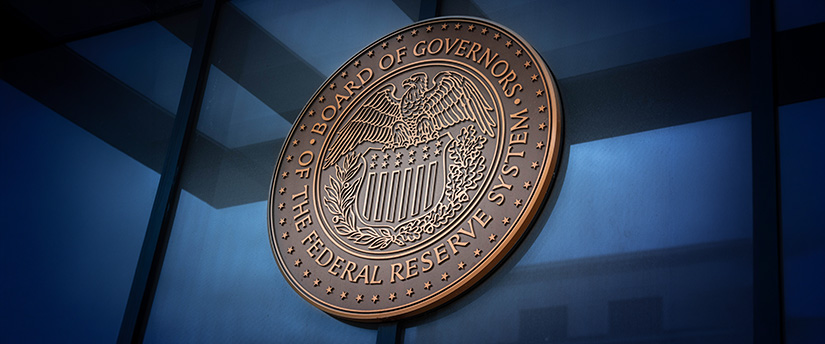 Close-up of the bronze Board of Governors of the Federal Reserve System seal mounted on a reflective blue glass window, symbolizing Federal Reserve Rate Cut Expectations 2026.